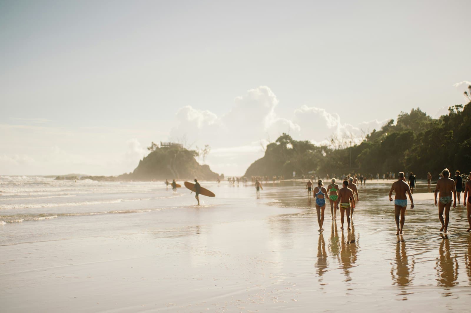 A surfer and beachgoers at The Pass in Byron Bay, in hazy golden light