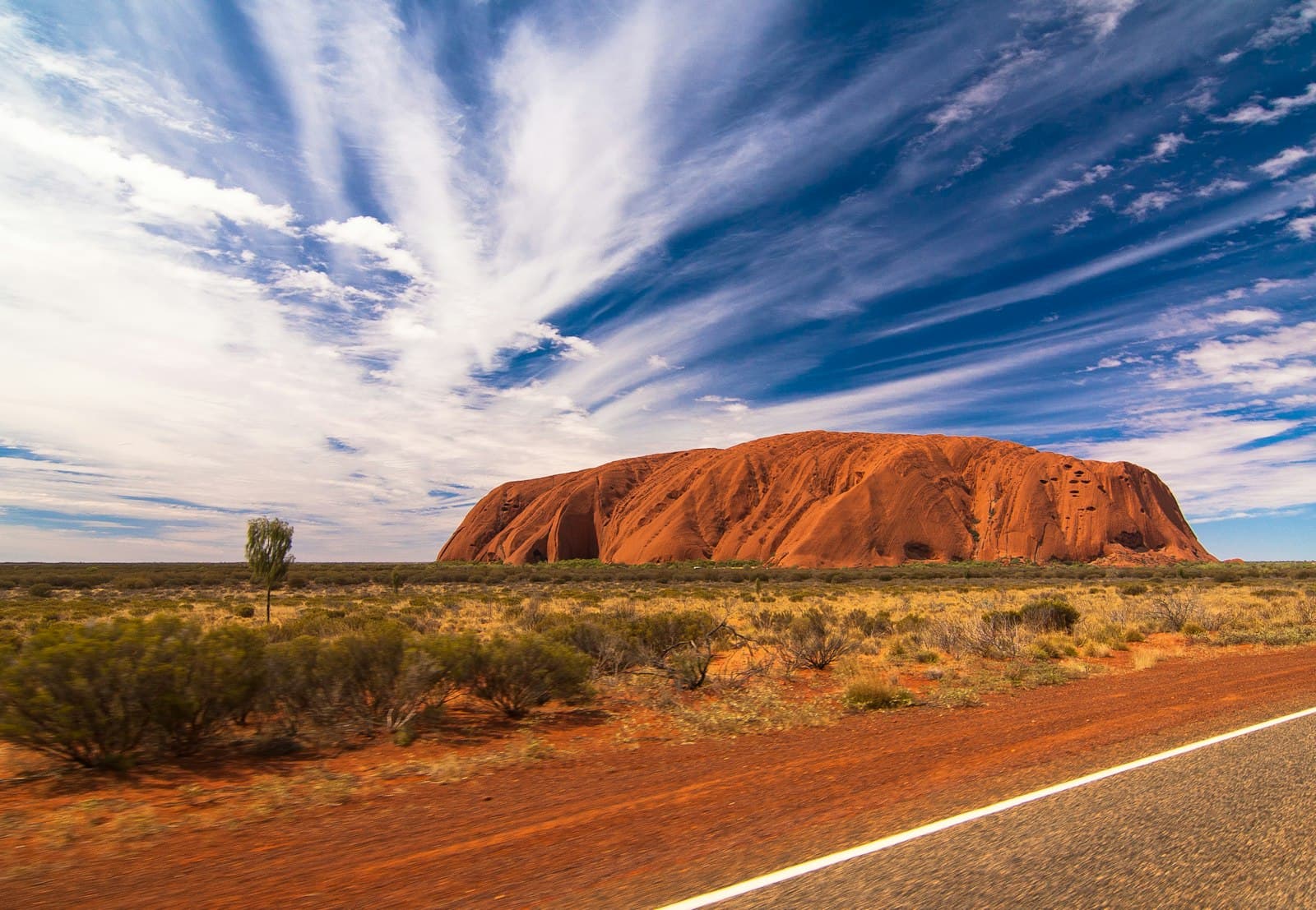 Uluru glowing red beneath a sky streaked with cloud