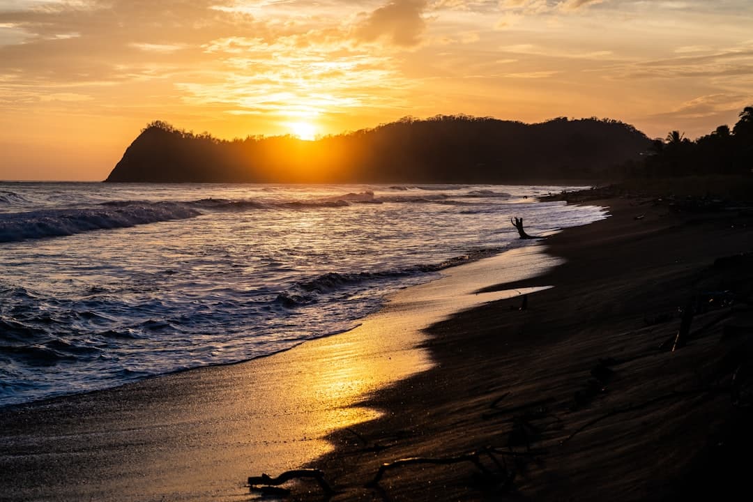 Golden sunset over a dark-sand Guanacaste beach beneath a forested headland