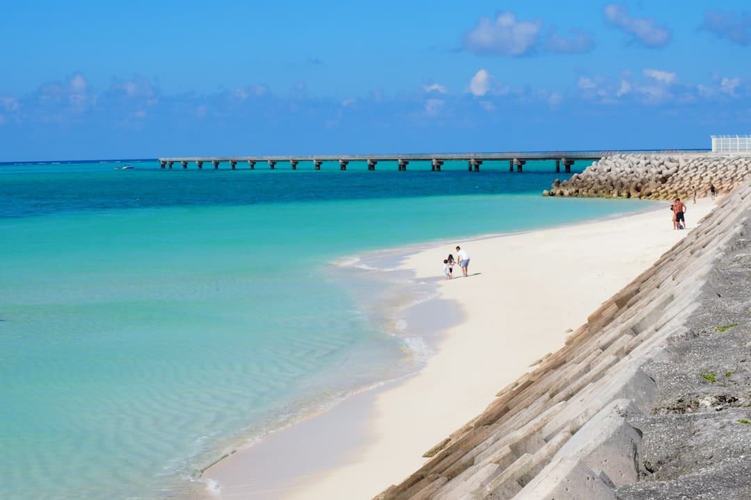 A white-sand Okinawan beach beside shallow turquoise water and a long pier