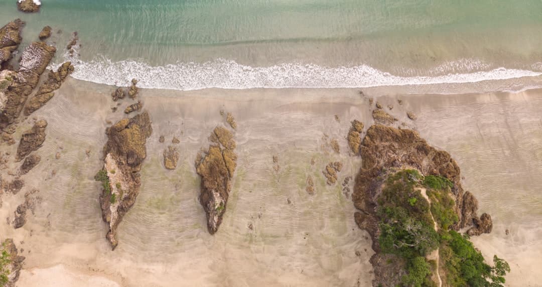 Aerial view of a sandy Waiheke Island beach with scattered rocks and gentle surf