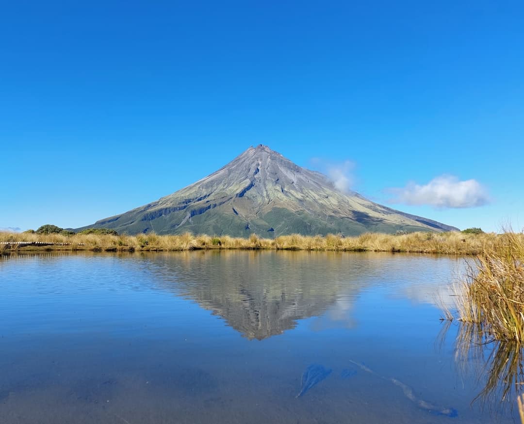 The snow-streaked cone of Mt Taranaki reflected perfectly in a still alpine tarn