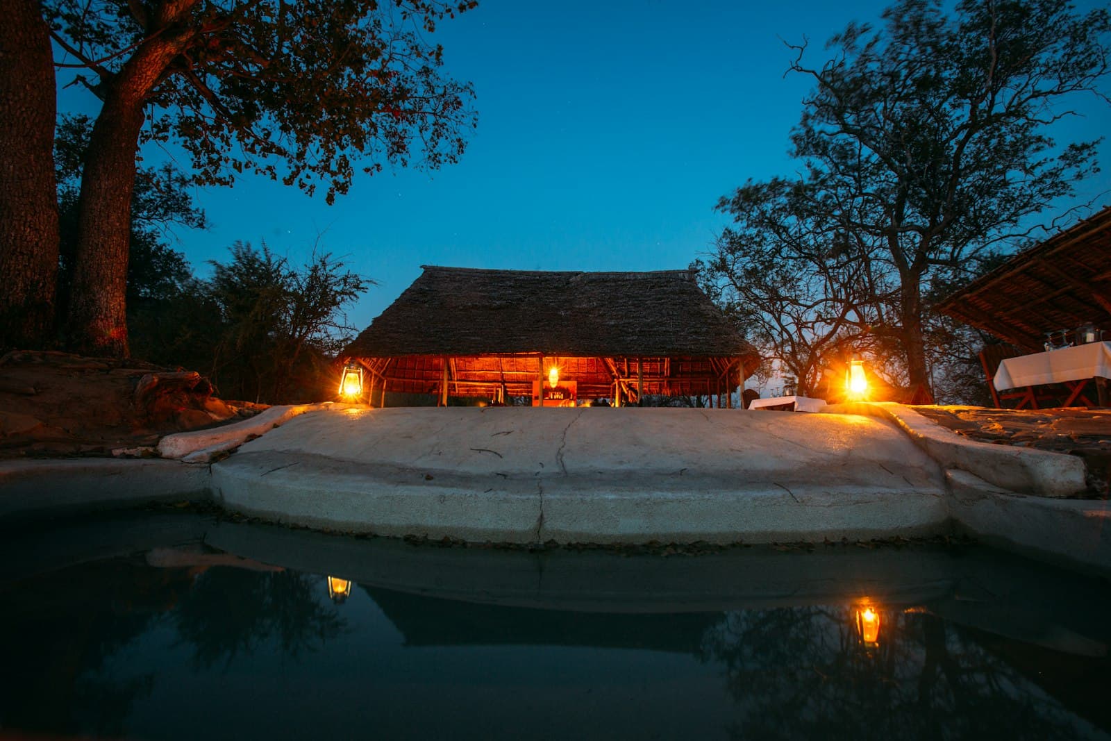 A lantern-lit safari lodge reflected in its pool at dusk