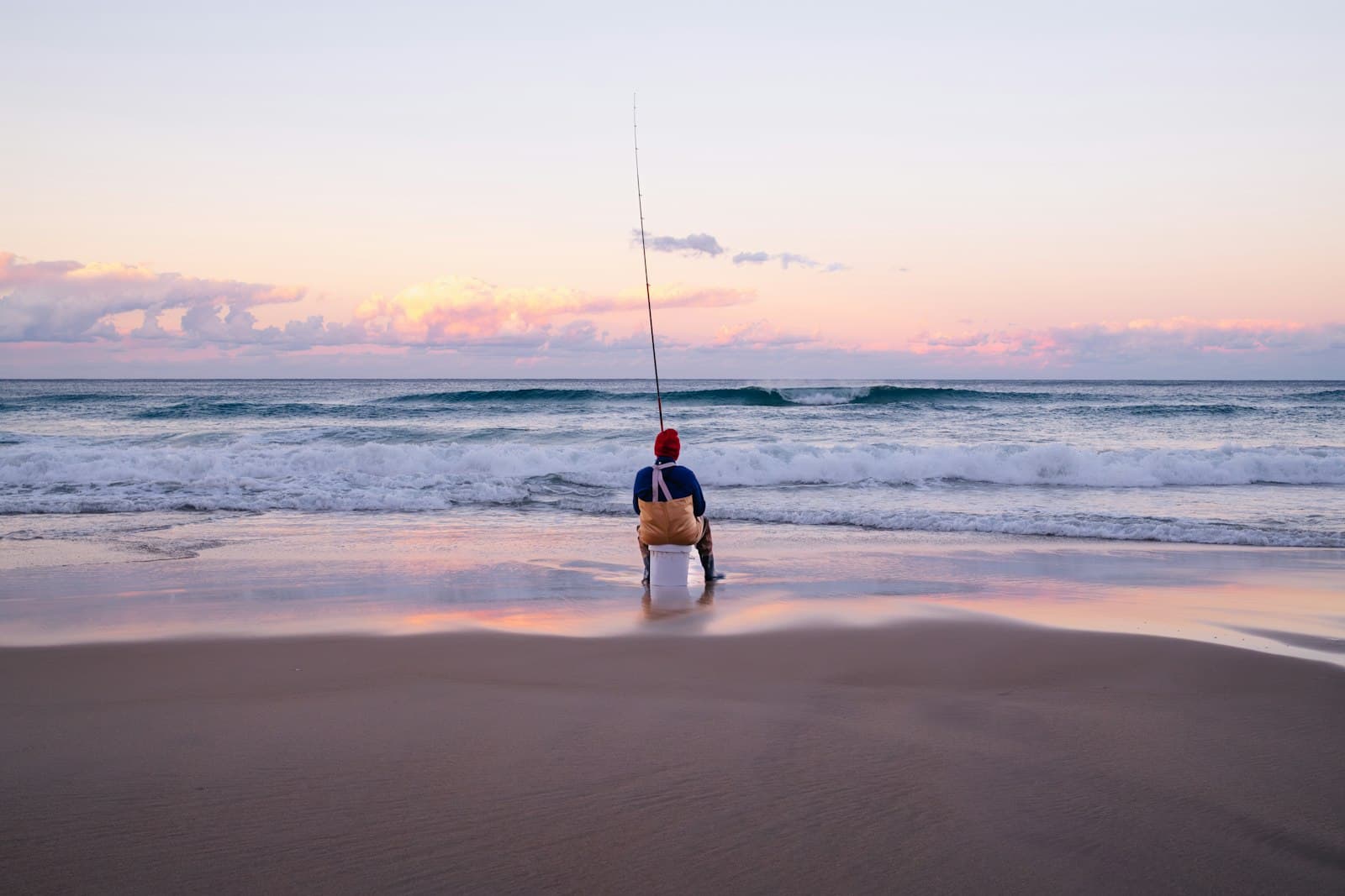 A fisherman casting into the surf at dusk
