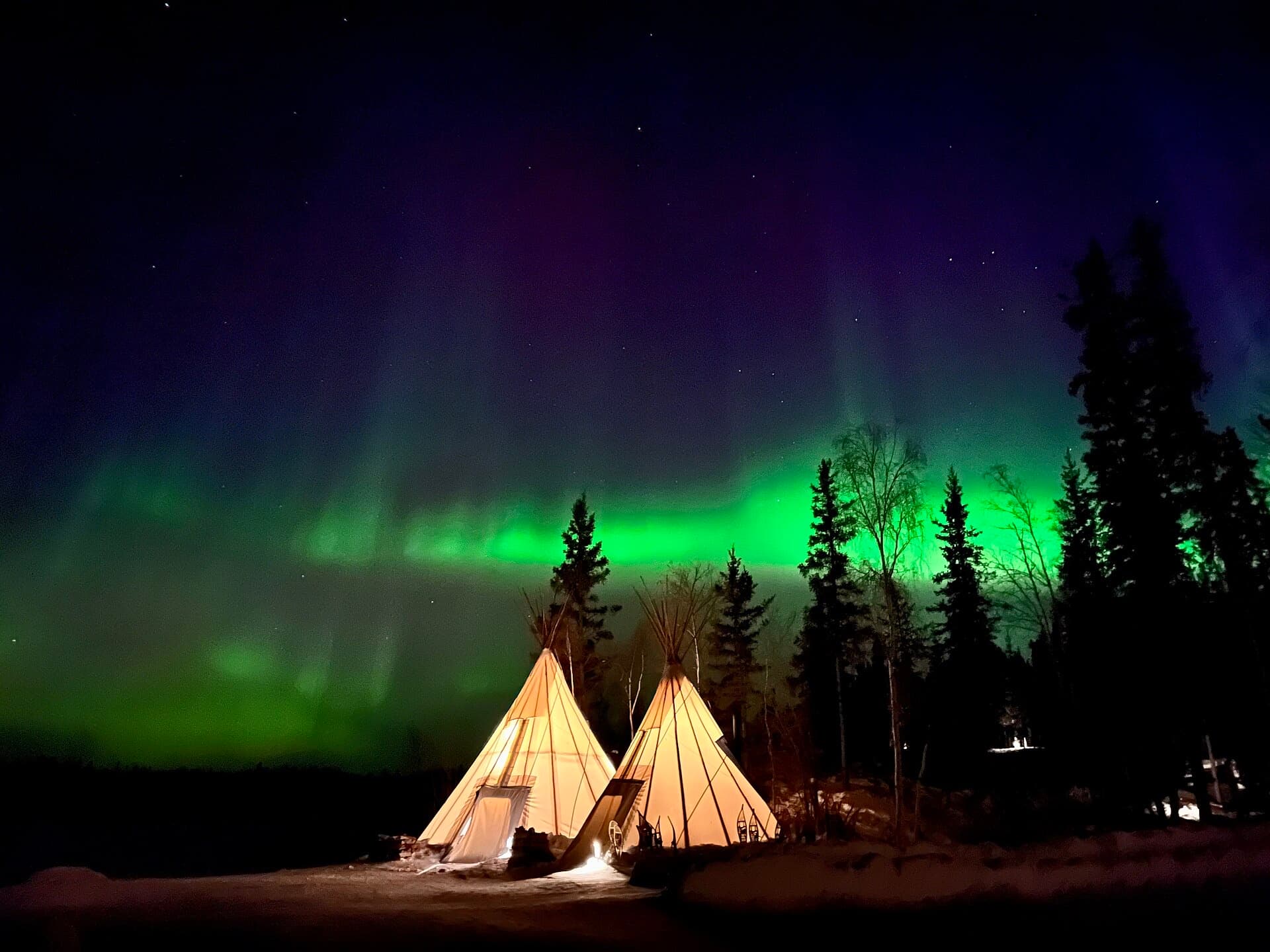 Green aurora curtains over lakeside teepees
