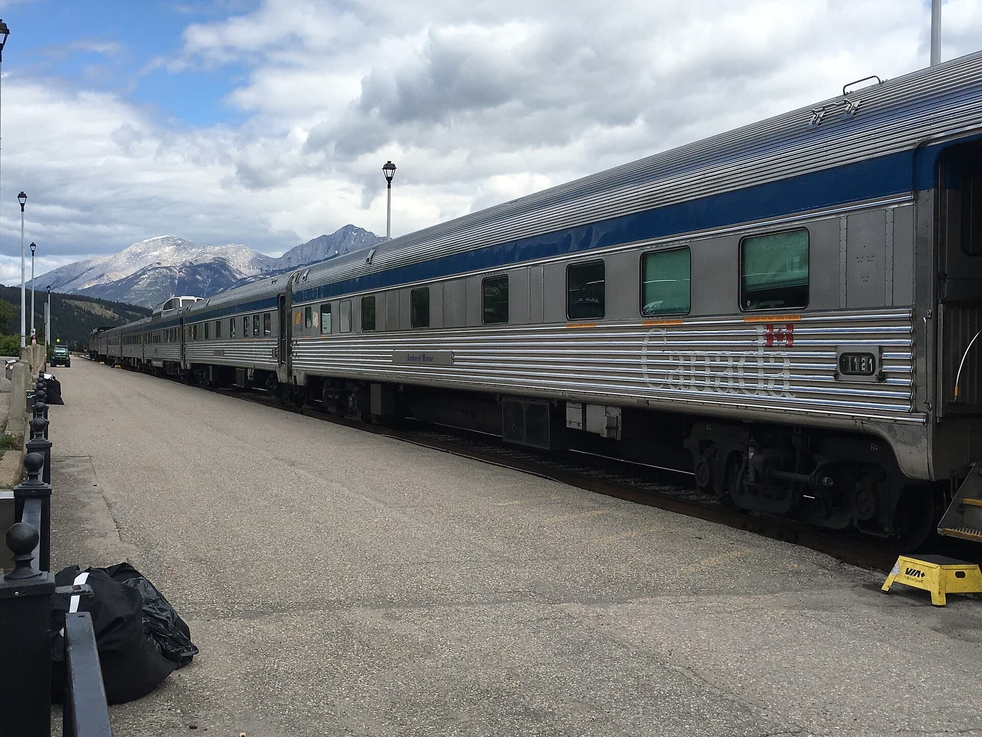 A silver transcontinental train waiting beneath Rockies peaks