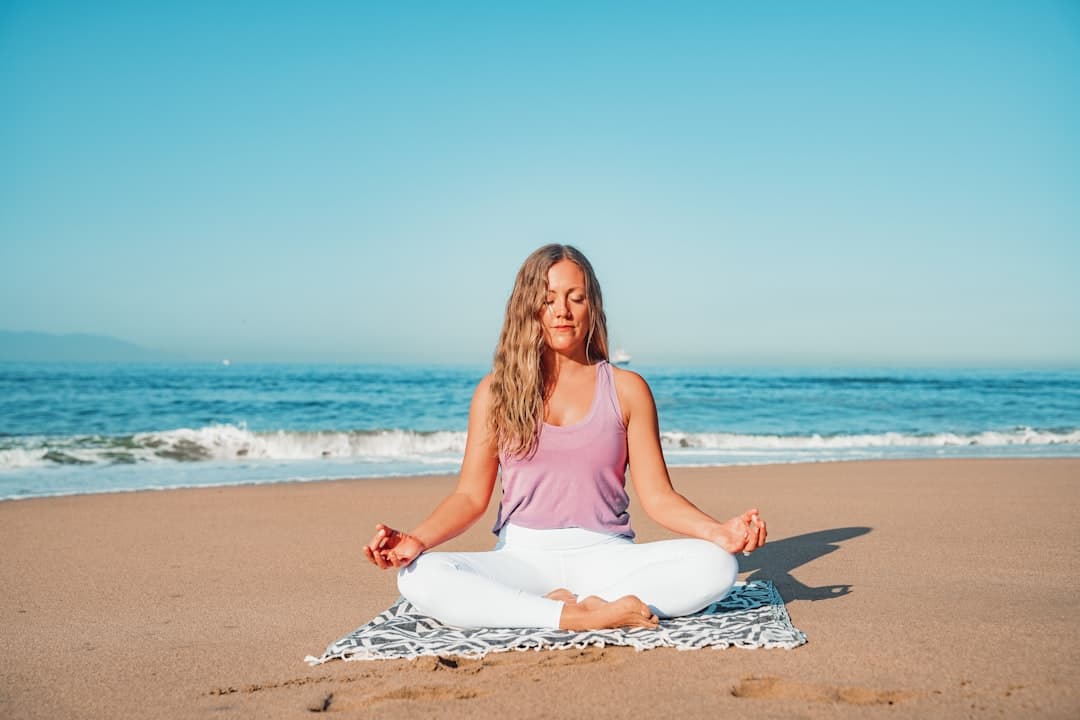 A woman meditating on the sand with gentle surf behind her
