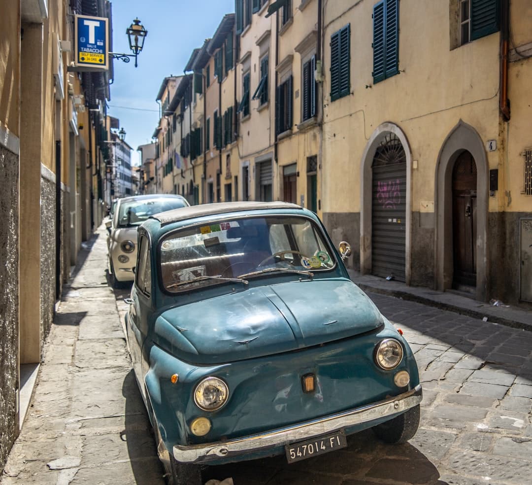 A teal vintage Fiat 500 on a narrow cobbled street