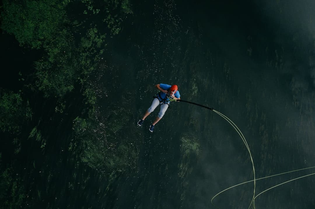 A bungy jumper dangling on the cord high above a green river gorge