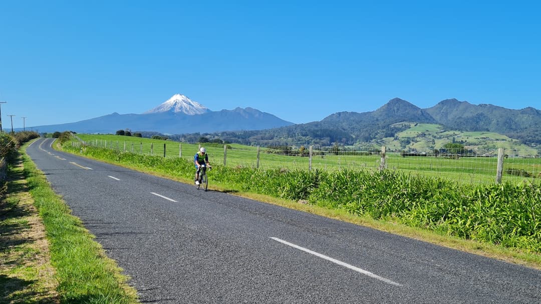 A cyclist on a quiet rural road with Mt Taranaki rising in the distance