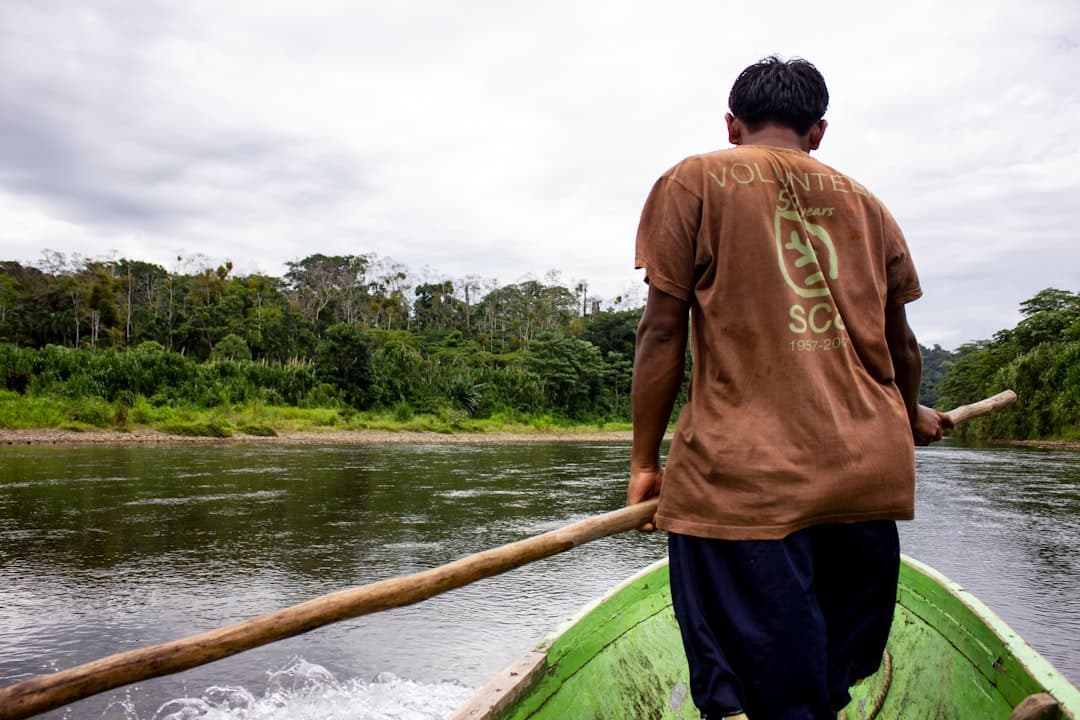A boatman poling a canoe along a jungle-lined waterway