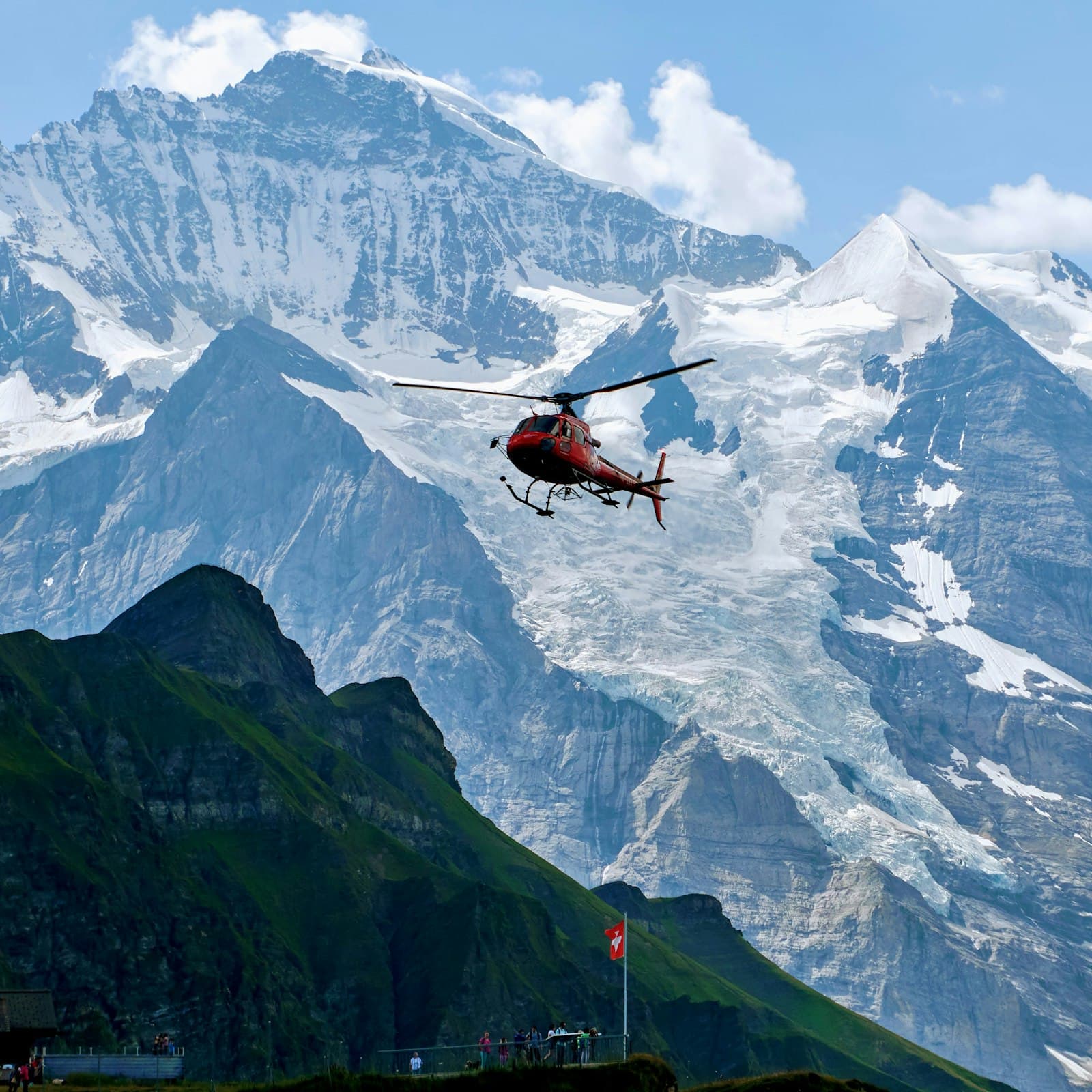 A red helicopter flying against glaciated alpine peaks