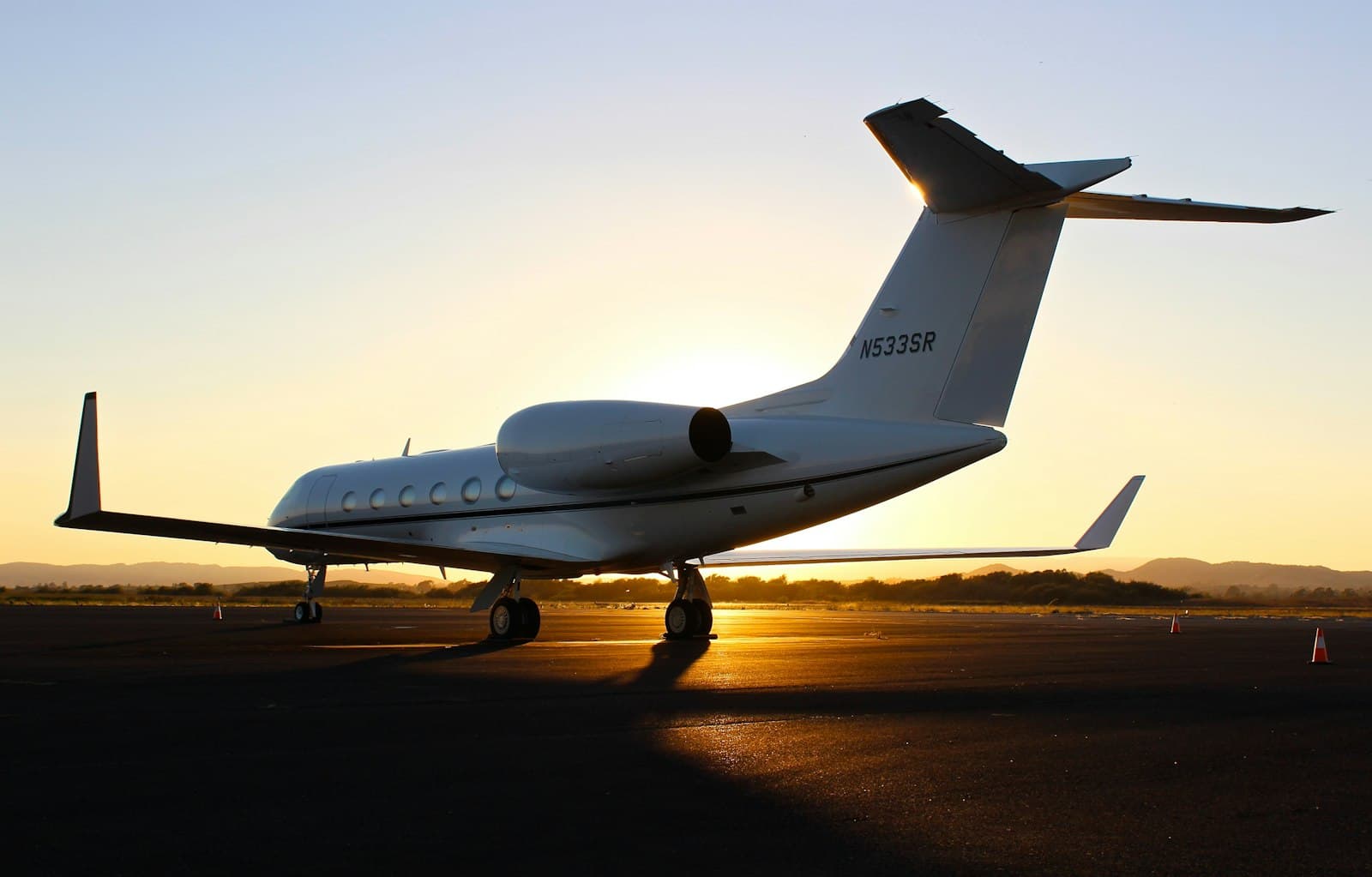 A private jet on the tarmac at sunset, sun flaring beneath the fuselage