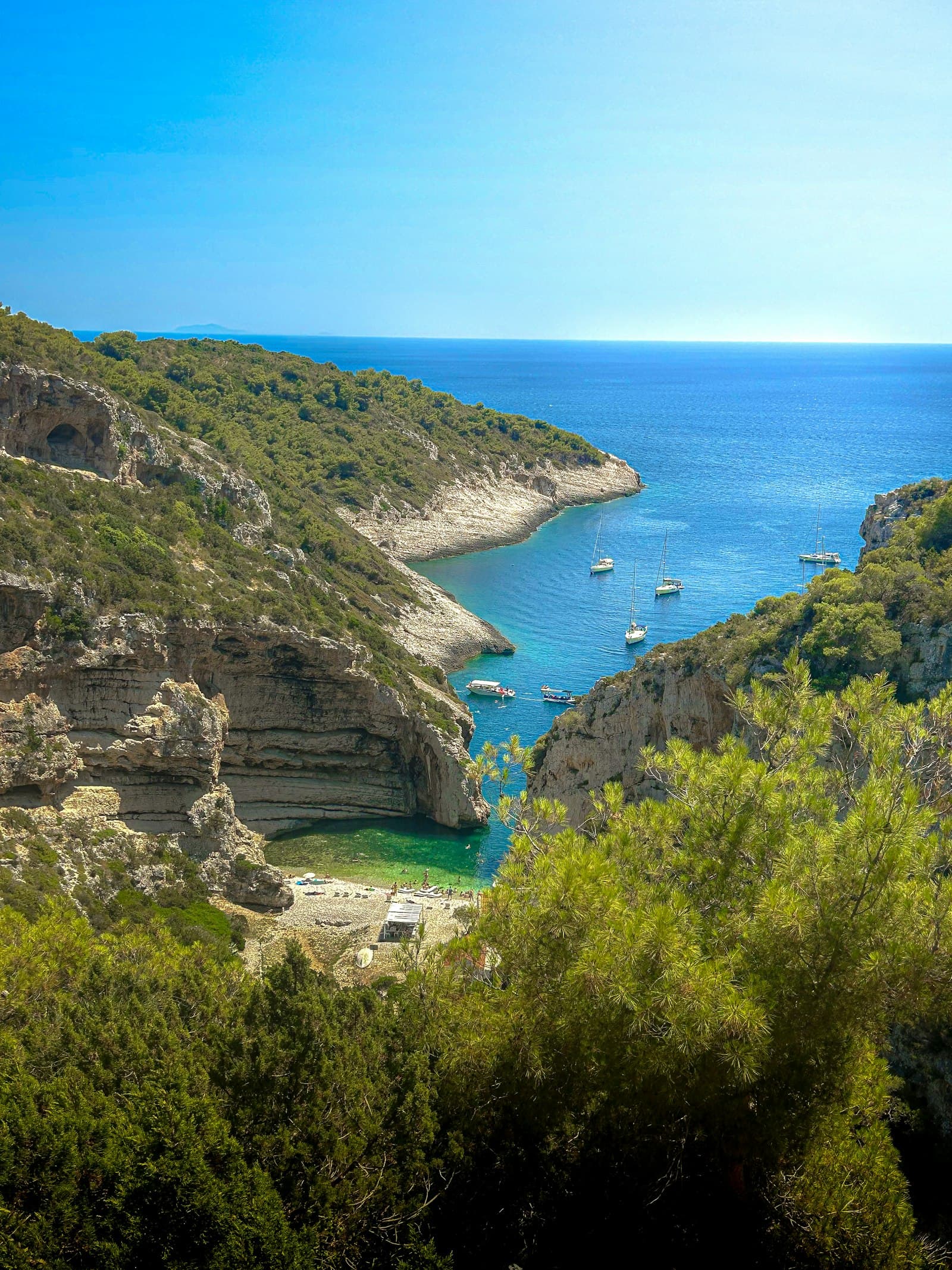 Sailing yachts anchored in a turquoise cove beneath limestone cliffs