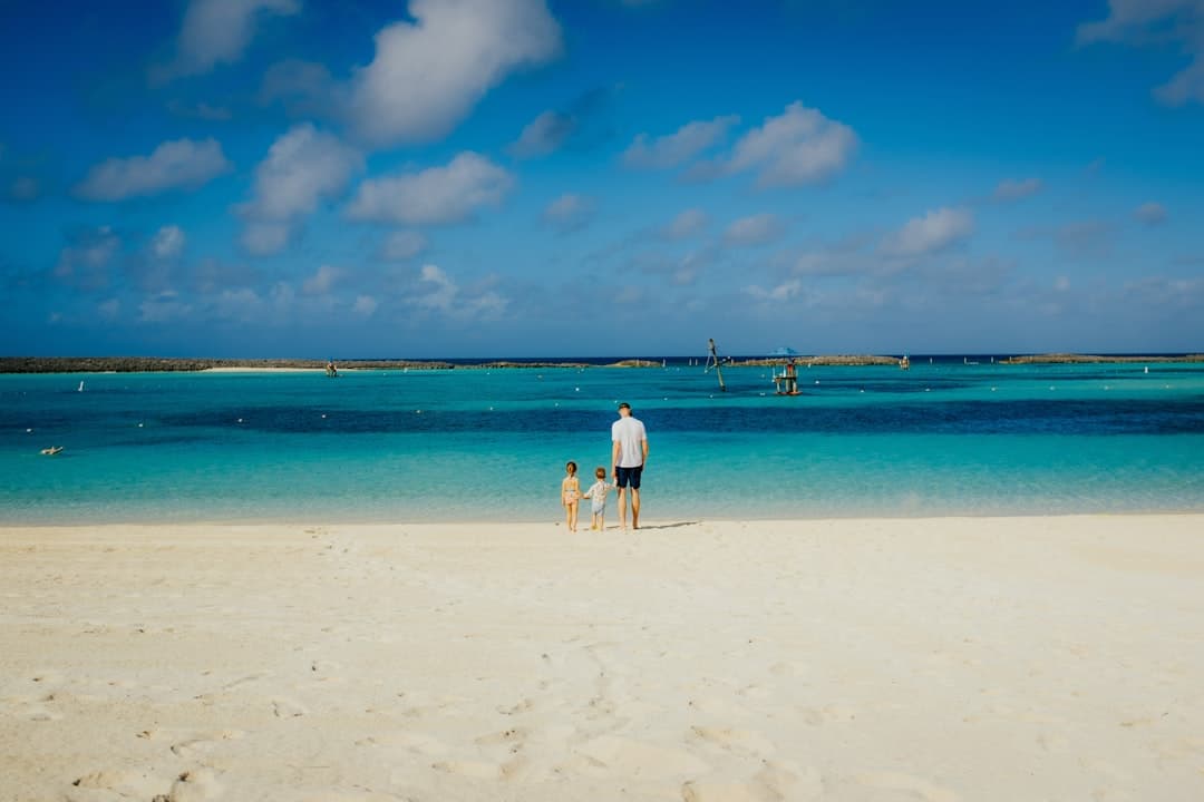 A parent and two children hand in hand at the edge of turquoise water